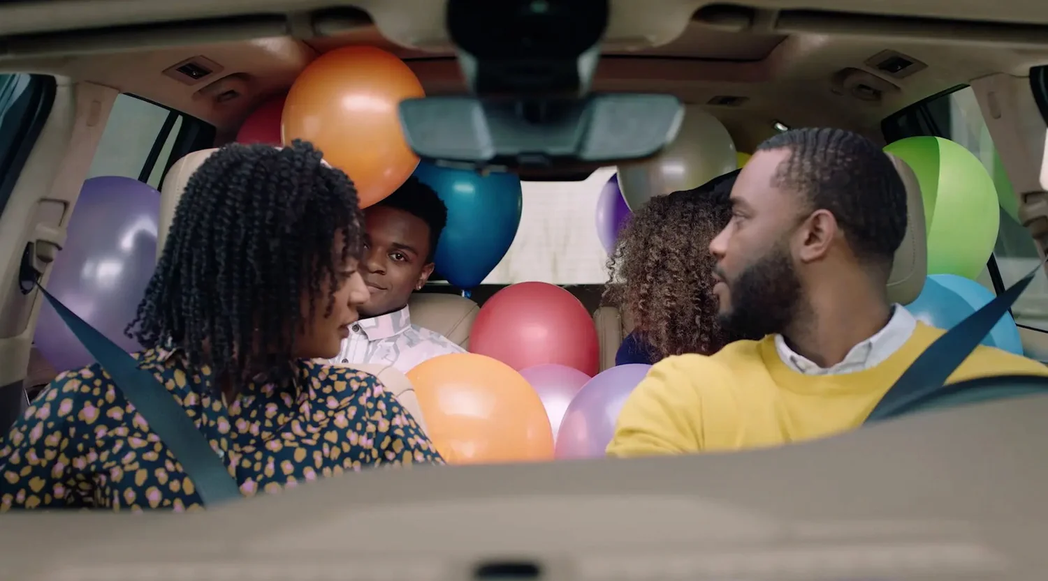 Lifestyle campaign image for Cadillac XT6 showing a family seated inside the vehicle surrounded by colorful balloons.