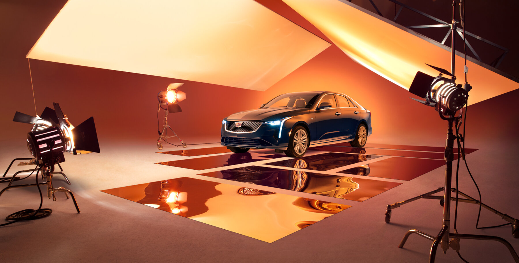 Cadillac campaign photography featuring a blue sedan on a reflective set with warm studio lighting.